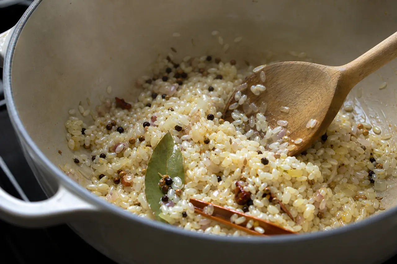 Épices entières, oignon et riz doucement nacrés dans une casserole